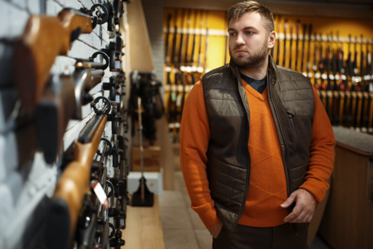 Man at showcase with rifles, back view, gun shop. Euqipment for hunters on stand in weapon store, hunting and sport shooting hobby